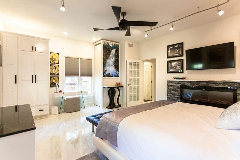 A modern bedroom featuring a large bed, a sleek wall-mounted TV, and natural light from windows.