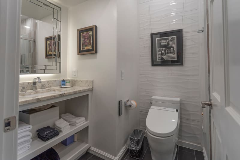 A modern bathroom featuring a sleek toilet, a granite vanity with toiletries, and neatly arranged towels.