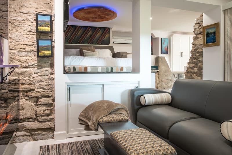 A cozy living space featuring a leather sofa, a stone wall, and a lofted bed area with decorative artwork.