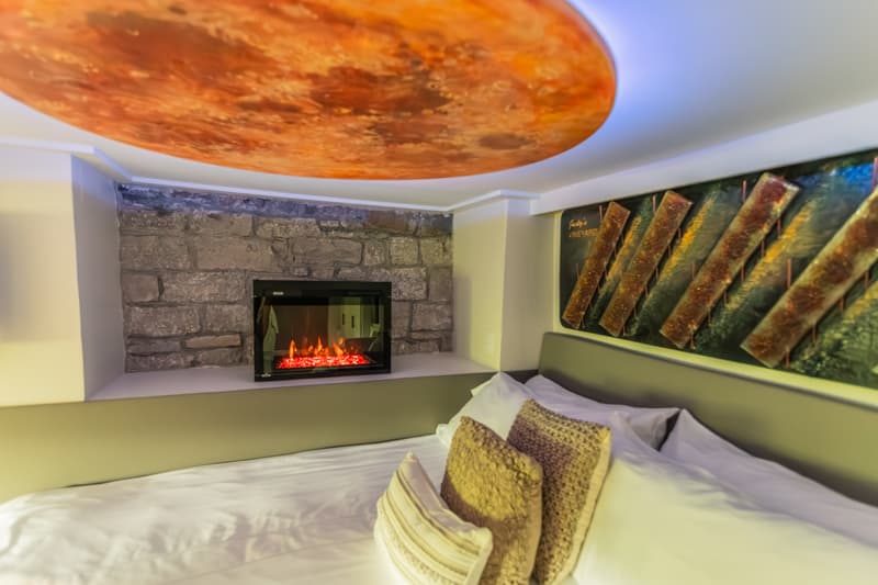 A cozy bedroom featuring a modern electric fireplace against a stone wall and decorative ceiling.