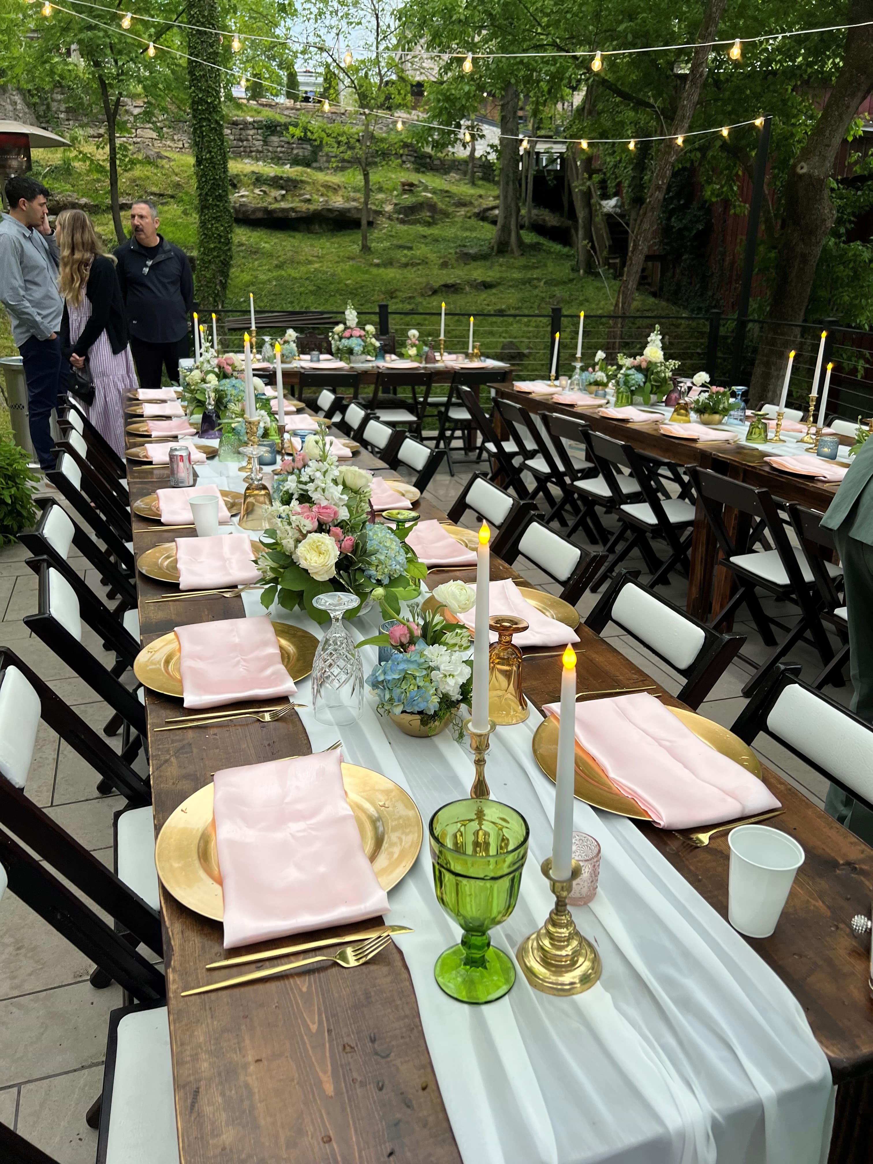 A beautifully arranged outdoor dining setting with elegant tableware, floral centerpieces, and candles.