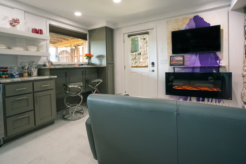 A modern kitchen and living area featuring a sleek design, bar stools, a mounted TV, and an electric fireplace.