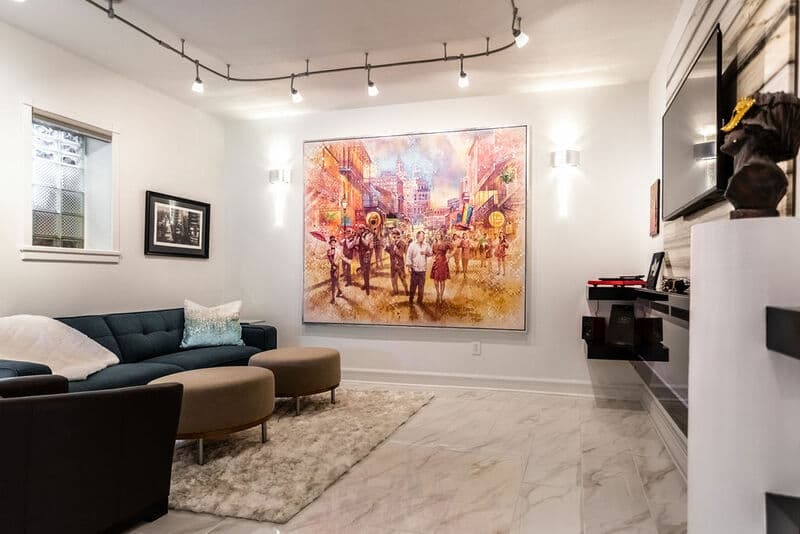 A modern living room featuring a blue couch, two round ottomans, and a large colorful painting on the wall.