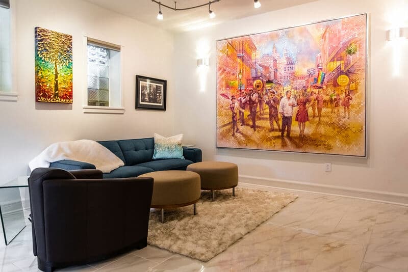 A cozy living room featuring a blue couch, two round ottomans, and a large colorful mural on the wall.