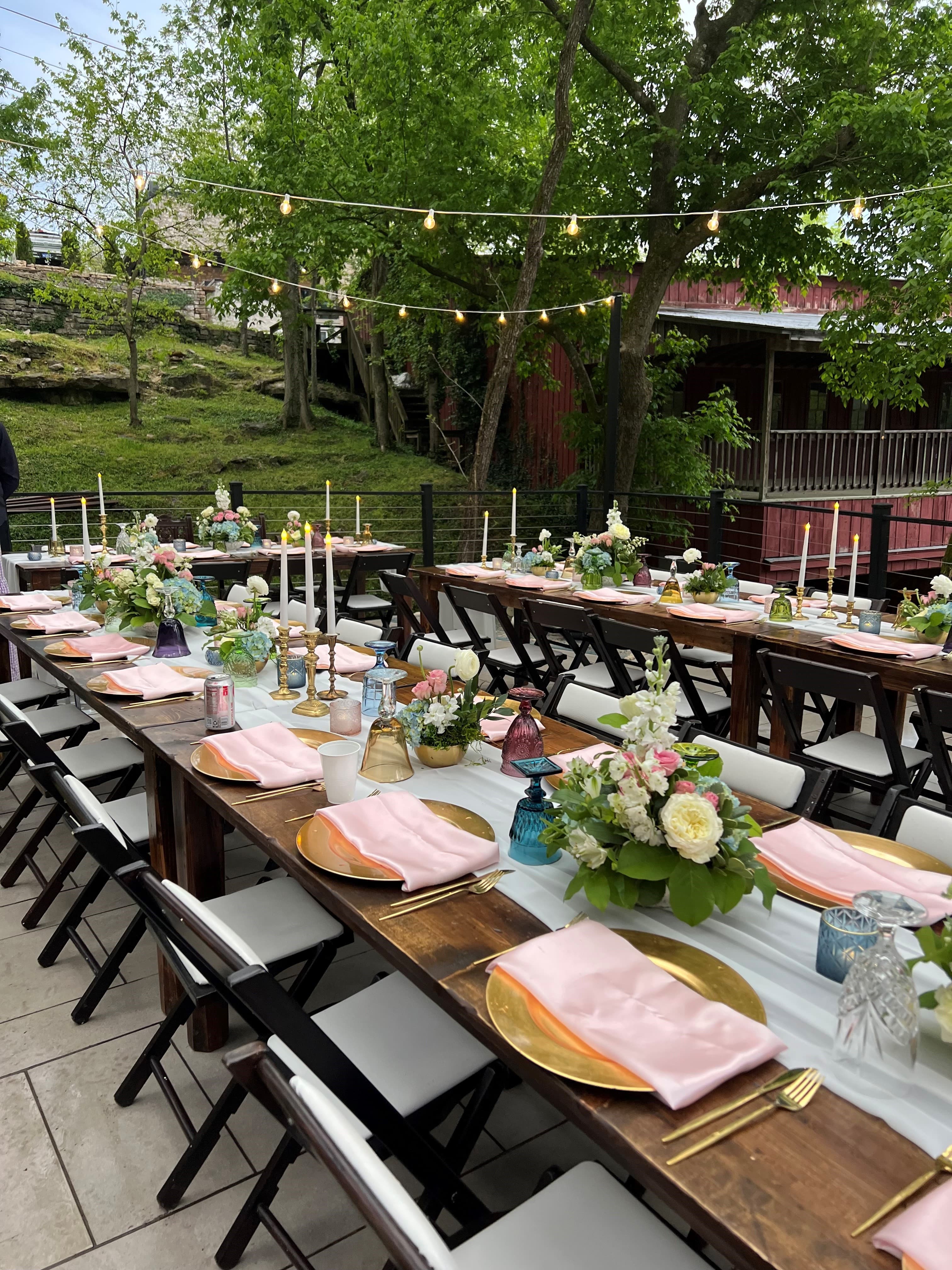 An elegantly set outdoor dining table adorned with floral centerpieces and candles, surrounded by greenery.