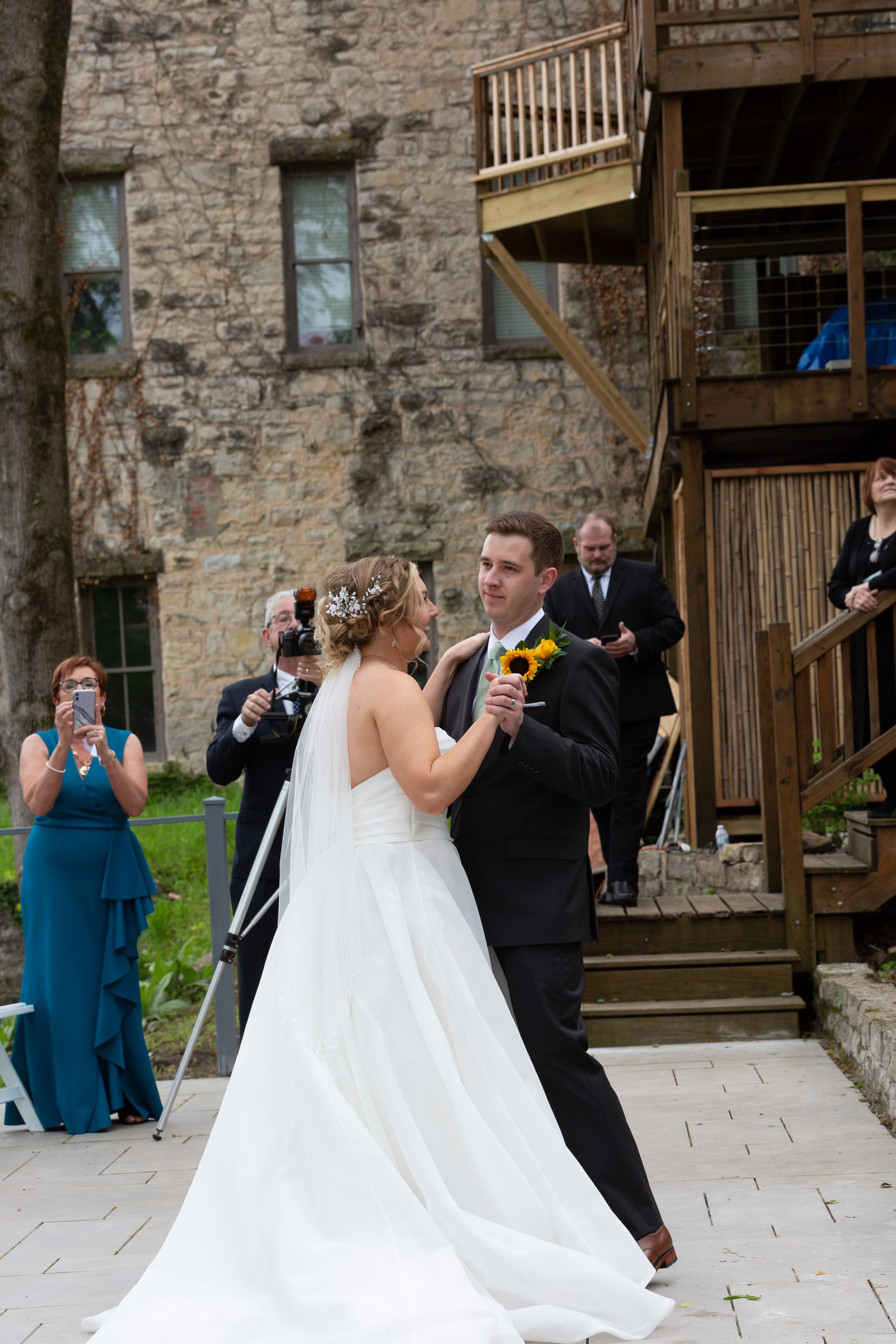 A bride and groom share their first dance at an outdoor wedding surrounded by guests.
