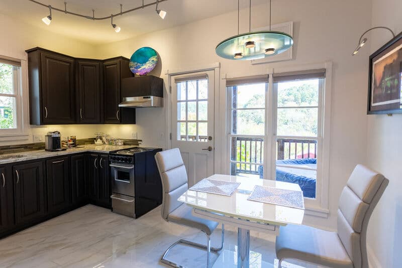 Modern kitchen and dining area with dark cabinets, a glass table, and natural light from a door leading to a balcony.