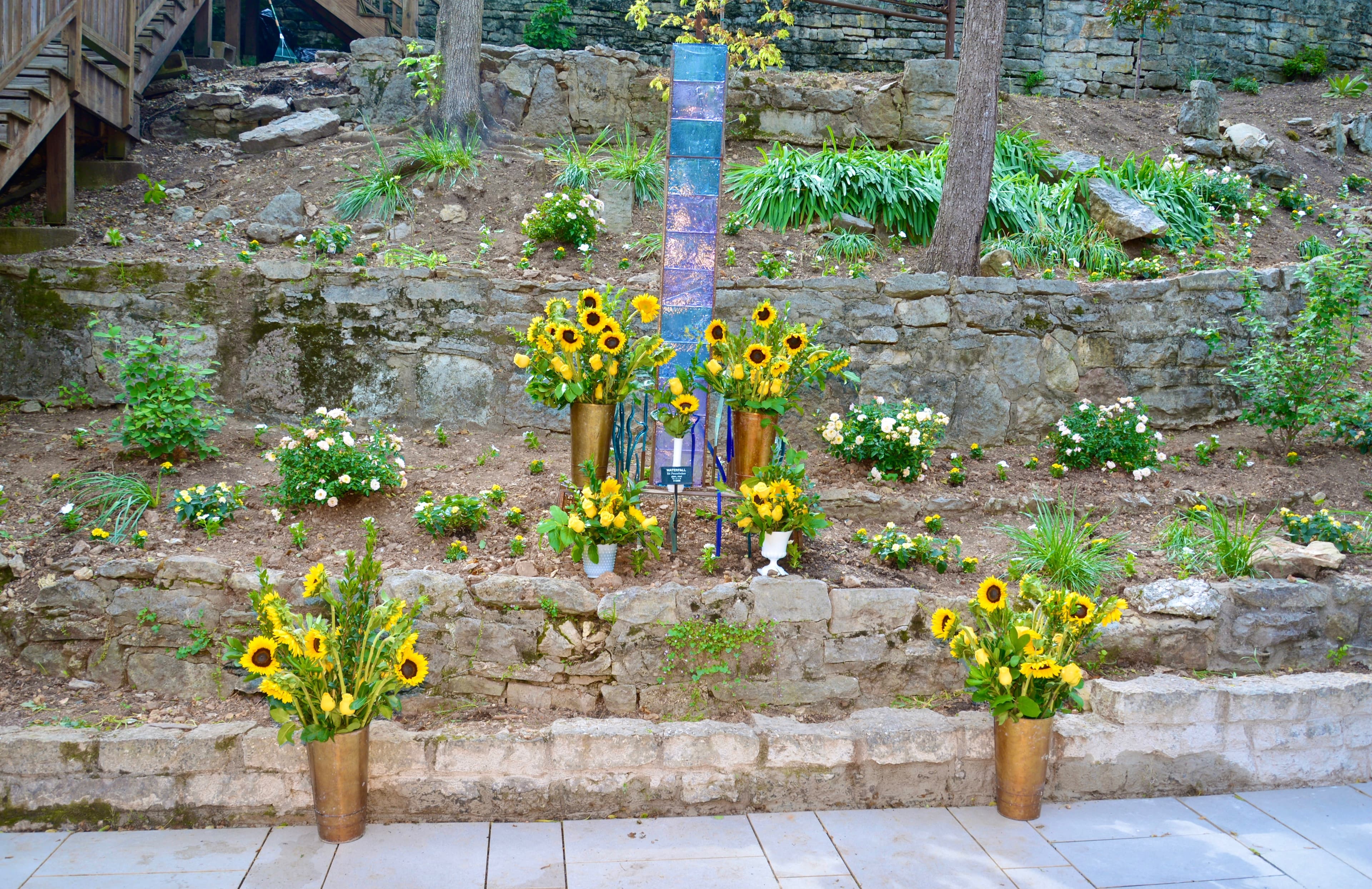 A stone garden features colorful arrangements of sunflowers and greenery.
