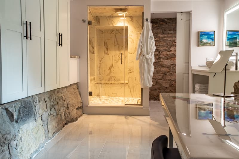 A modern bathroom featuring a glass shower, marble walls, and a stone accent wall.