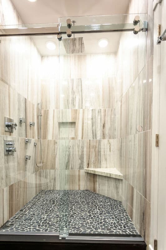 A modern glass shower featuring striped tile walls and a pebble stone floor.