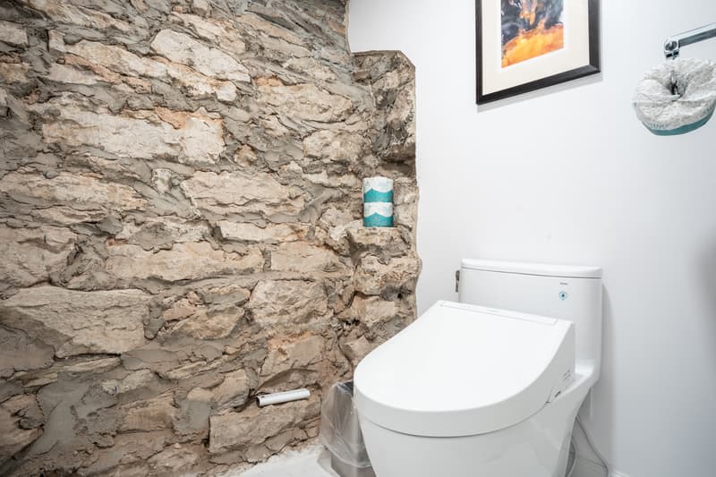 A modern toilet is situated beside a textured stone wall in a minimalist bathroom.