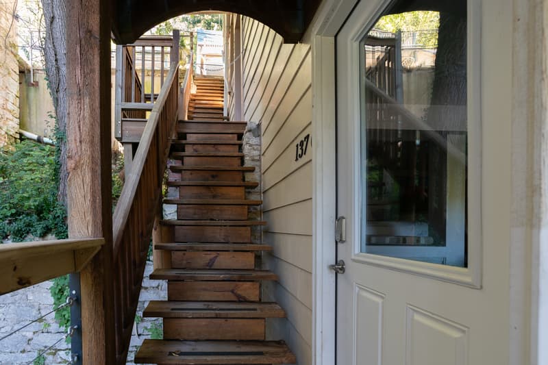 A view of wooden stairs leading up to a door marked "137" beside a wall.